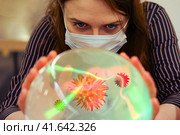 A woman is wondering about the future of the coronavirus on a ball of fate. Masked witch girl over crystal ball predicts the future of flu virus. Стоковое фото, фотограф Андрей Журавлев / Фотобанк Лори