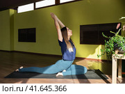 Молодая привлекательная шатенка практикующая йогу, выполняющая упражнения Эка Пада Раджакапотасана, позу голубя, тренирующаяся в спортивной одежде сидя на коврике в студии. Стоковое фото, фотограф Сергей Чайко / Фотобанк Лори