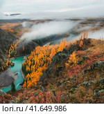 Colorful view to autumn mountain valley with forest and river against mountain range under cloudy sky. Wide mountain valley in mist and large mountains in lush clouds in changeable weather. Стоковое фото, фотограф Саблин Станислав / Фотобанк Лори