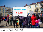 Мужчина несет плакат с надписью "Да здравствует 1 мая!". Первомайская демонстрация. Митинг и праздничное шествие по улице города. Магадан, Магаданская область, Россия. (2018 год). Редакционное фото, фотограф Андрей Степанов / Фотобанк Лори