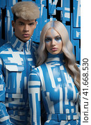 A young smiling cheerful couple, two friends, a family man and a woman in unusual blue designer clothes, stand next to each other, directing their gaze at the camera. Generated by AI. Стоковое AI-изображение, AI-художник Ярославский Максим / Фотобанк Лори