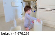 A child is playing with chemical cleaning products under the sink in the kitchen. Baby holds bottles with detergent. Kid aged about two years (one year nine months) Стоковое видео, видеограф Андрей Журавлев / Фотобанк Лори