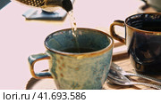 Brewing and Serving Tea. Teapot Pouring Green Tea in Blue Ceramic Cup on Wooden Cafe Table. Two Pottery Handmade Mugs Early in the Morning. Trendy Authentic Porcelain Set. Breakfast Concept. Tea Time. Стоковое видео, видеограф Марина Демидюк / Фотобанк Лори