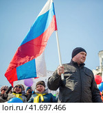 Мужчина с российским флагом и счастливые женщины во время праздничной первомайской демонстрации. Радостное праздничное настроение. Патриоты России на митинге 1 мая, в День труда. Магадан, Магаданская область, Россия. (2018 год). Редакционное фото, фотограф Андрей Степанов / Фотобанк Лори