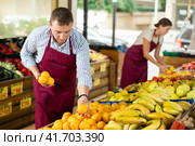 Male seller of vegetable department of store is replenishing showcase with oranges. Стоковое фото, фотограф Яков Филимонов / Фотобанк Лори