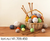 Woolen clews of warm soft wool yarn in wicker basket with wooden knitting needles and crochet hook on wooden table. Rustic still life. Needlework, hobbies and knitting. DIY concept. Closeup, copy space. Стоковое фото, фотограф Виктория Катьянова / Фотобанк Лори