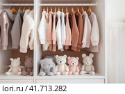 Kid's clothes hanging on hangers on rails and toys in white wooden wardrobe in the children's room. Стоковое AI-изображение, AI-художник Оксана Гильман / Фотобанк Лори