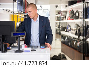 Concentrated man standing at a computer in a store, specifying the price of the desired goods. Стоковое фото, фотограф Яков Филимонов / Фотобанк Лори