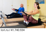 Woman pulling stretch band sitting on pilates training machin. Стоковое фото, фотограф Яков Филимонов / Фотобанк Лори