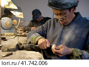 Косторез вырезает скульптуру из моржового клыка. Уэленская косторезная мастерская, Уэлен, Чукотка, Россия. Традиционное чукотское искусство резьбы по кости. Искусство народов Арктики. Редакционное фото, фотограф Андрей Степанов / Фотобанк Лори