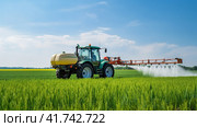 Watering, treating fields with crops with Pesticides and Herbicides on a tractor. Agricultural industry. Стоковое AI-изображение, AI-художник Ирина Ручушкина / Фотобанк Лори