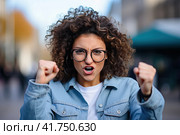 A young girl with curly hair rejoices in luck with her fists raised up. Generated by AI. Стоковое AI-изображение, AI-художник Ярославский Максим / Фотобанк Лори