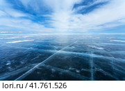 A harsh winter landscape of a lifeless endless icy desert of a frozen sea and beautiful layered clouds above it. Cold natural background of Siberian Baikal Lake with snow-capped mountains in the distance. Стоковое фото, фотограф Виктория Катьянова / Фотобанк Лори