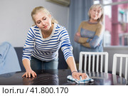 Elderly mother is unhappy with the way her adult daughter dusts the table in room. Стоковое фото, фотограф Яков Филимонов / Фотобанк Лори
