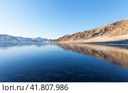 Winter landscape of frozen Baikal Lake in January at sunset. Tourists come to shore of iced bay to walk on clean thin ice and go ice skating. Winter active ice travel and outdoors. Empty space for text. Стоковое фото, фотограф Виктория Катьянова / Фотобанк Лори
