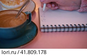 Woman Writing Plan in a Notepad Sitting on a Pink Cafe Table with Coffee Cup and Dessert. Hand Close up. New Year Routine, Resolution. Goals, To Do List in the Notebook. Action, Checklist Idea Concept. Стоковое видео, видеограф Марина Демидюк / Фотобанк Лори