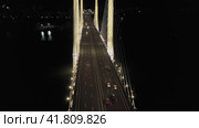 A cable-stayed highway bridge with tall concrete pylons illuminated by architectural lighting at night. Orbital overflight over the road (2023 год). Редакционное видео, видеограф Даниил Хабаров / Фотобанк Лори