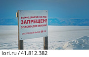 Warning of the prohibition to go out on the ice. Danger to life. A wooden sign in Russian on the shore of Lake Baikal against the background of the mountains in winter. Siberia, Russia. (2022 год). Редакционное видео, видеограф Даниил Хабаров / Фотобанк Лори