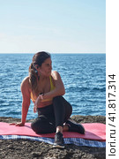 Latin woman, middle-aged, resting, regaining strength, eating, drinking water, after a gym session, wearing orange top, burning calories, keeping fit, outdoors by the sea, blue sky, beautiful day , sunny winter, Bluetooth headphones, and smart watch. Стоковое фото, фотограф carlos l vives / Фотобанк Лори