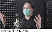 A man in a medical mask sings at a microphone in a recording studio. Quarantine in the recording studio and music small business due to problems with the virus. Стоковое видео, видеограф Андрей Журавлев / Фотобанк Лори