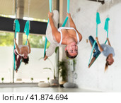 Young European woman doing exercise in hammock in antigravity yoga studio. Female group workout for health. Стоковое фото, фотограф Яков Филимонов / Фотобанк Лори