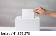 The person places a ballot for the election of president, senator or deputy into a white ballot box. Стоковое AI-изображение, AI-художник ALLA YURTAYEVA / Фотобанк Лори