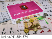 Долговой документ за неуплату жилищно-коммунальных услуг (ЖКУ), российские деньги-банкноты и монеты лежат на листках календаря. Стоковое фото, фотограф Владимир Устенко / Фотобанк Лори