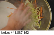 A close-up of a woman's hand from a white plate places sliced carrots and radishes, in chunks of meat and onions frying in a cauldron. The liquid in the wok is boiling and steam is rising. Стоковое видео, видеограф Воловодов Владимир / Фотобанк Лори