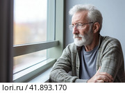 A man sitting at the window of a hospital room, with a sad look. Стоковое AI-изображение, AI-художник Юрий Поздников / Фотобанк Лори