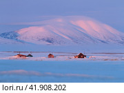 Winter landscape with snow-covered houses and a mountain. Soft morning light. Abandoned cottages in the tundra. Cold May in the Arctic. Chukotka, Siberia, Far East of Russia. Стоковое фото, фотограф Андрей Степанов / Фотобанк Лори