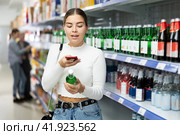 Young girl scanning barcode on bottle of soju with smartphone at Asian store. Стоковое фото, фотограф Яков Филимонов / Фотобанк Лори