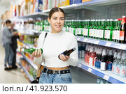 Young girl examining labels on bottles of soju in Asian store. Стоковое фото, фотограф Яков Филимонов / Фотобанк Лори