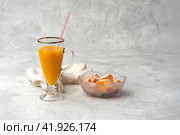 Pumpkin diet. Glass with drinking straw smoothie and plate with pumpkin cubes in coconut crumble on gray textured background. Focus stacking. Copy space. Стоковое фото, фотограф Роман Дзюбало / Фотобанк Лори