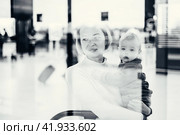 Thoughtful young mother looking trough window holding his infant baby boy child while waiting to board an airplane at airport terminal departure gates. Travel with baby concept. Стоковое фото, фотограф Matej Kastelic / Фотобанк Лори