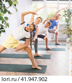 School children and their parents exercising on mats in Extended Side Angle Pose or Utthita Parsvakonasana during family yoga training in gym. Стоковое фото, фотограф Яков Филимонов / Фотобанк Лори