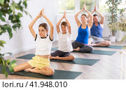 Pleasant preteen girl practicing half lotus pose of yoga with her family. Стоковое фото, фотограф Яков Филимонов / Фотобанк Лори