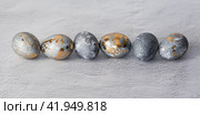 Stylish grey Easter eggs made of marble and concrete with a golden potala on a grey background. Coloring eggs with natural dye karkade tea. Environmental friendliness. Naturalness. The concept of a happy Easter. (2023 год). Стоковое фото, фотограф Photojuli / Фотобанк Лори