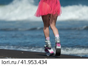 Rear view of fit female legs in short skirt and sports jumping boots Kangoo Jumps running on beach during training fitness session. Low section, crop view (2022 год). Редакционное фото, фотограф А. А. Пирагис / Фотобанк Лори