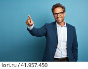 A handsome young man in a business suit and glasses points to the side with his right hand and smiles. Стоковое AI-изображение, AI-художник Ярославский Максим / Фотобанк Лори