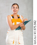 Happy emotional woman in overalls making entries in invoice or warrant. Стоковое фото, фотограф Яков Филимонов / Фотобанк Лори