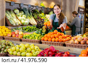 Female seller holding mandarin oranges standing in fruit and vegetable section of supermarket. Стоковое фото, фотограф Яков Филимонов / Фотобанк Лори