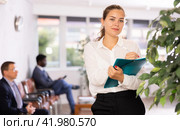 Friendly hostess woman stands at office reception with list of guests and expects invited visitors. Стоковое фото, фотограф Яков Филимонов / Фотобанк Лори