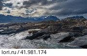Sea lions lie on the slope of a rocky islet. Cormorants have settled on the cliffs, flying. A picturesque mountain range of the Andes against a cloudy sky.Turquoise waves are beating against the rocks. Стоковое фото, фотограф Вера Ивановна Кубарева / Фотобанк Лори