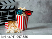 A banner for the film industry. A movie date. A movie camera, 3D glasses, popcorn in striped cups on a stylish concrete gray background. The premiere of the film. (2024 год). Стоковое фото, фотограф Photojuli / Фотобанк Лори