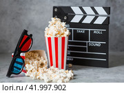 A banner for the film industry. A movie date. A movie camera, 3D glasses, popcorn in striped cups on a stylish concrete gray background. The premiere of the film. (2024 год). Стоковое фото, фотограф Photojuli / Фотобанк Лори