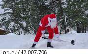Santa Claus cleans snow with shovel in winter outdoors after a snowfall. Cleaning the streets in the village, clearing the passage for cars, difficult weather conditions for Christmas and New Year. Стоковое видео, видеограф Ольга Симонова / Фотобанк Лори