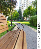 Summer city: a cozy bench, covered with boards and adorned with ornate iron handles, on a beautified square in the warm afternoon light. The bench' straight lines continue into the path' curved lines (2023 год). Стоковое фото, фотограф Анатолий Власов / Фотобанк Лори