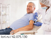Female nurse in disposable cap and mask injects vaccine into shoulder of elderly male patient. Стоковое фото, фотограф Яков Филимонов / Фотобанк Лори