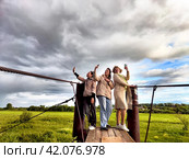 Three funny tourist girls on the old bridge take selfies against the background of an alarming dramatic sky with thunderclouds. Middle-aged women having fun outdoors. Стоковое фото, фотограф Кривошеина Елена Леонидовна / Фотобанк Лори
