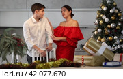 Upset young couple arguing among themselves before X-mas Eve near Christmas tree in kitchen at home. Стоковое видео, видеограф Яков Филимонов / Фотобанк Лори